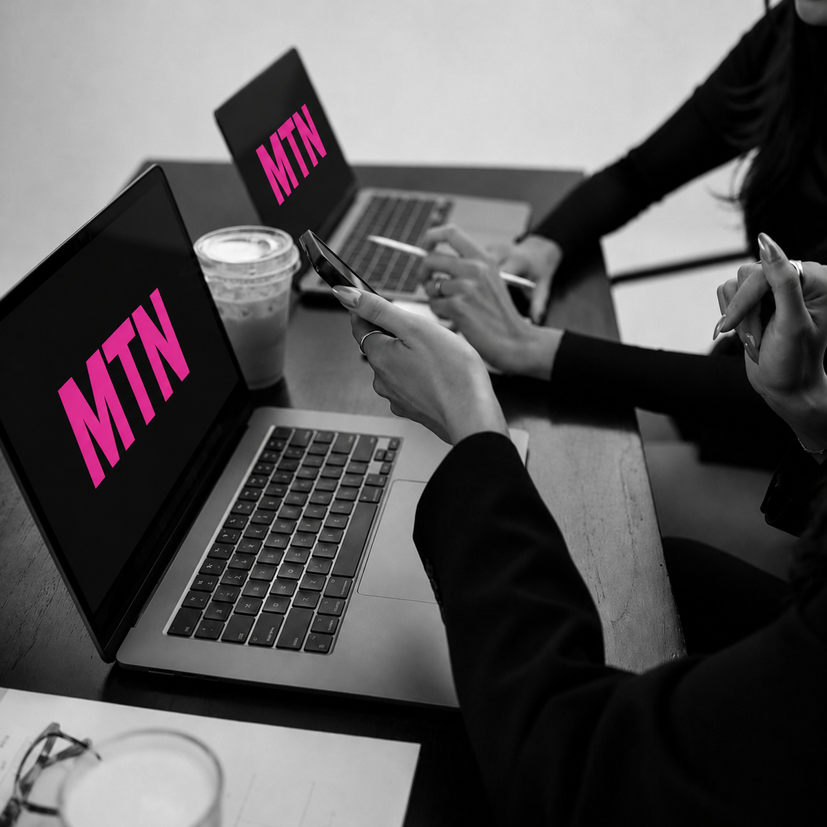 Two laptops open on a desk, each featuring a bright pink MTN campaign logo on the outer shell.