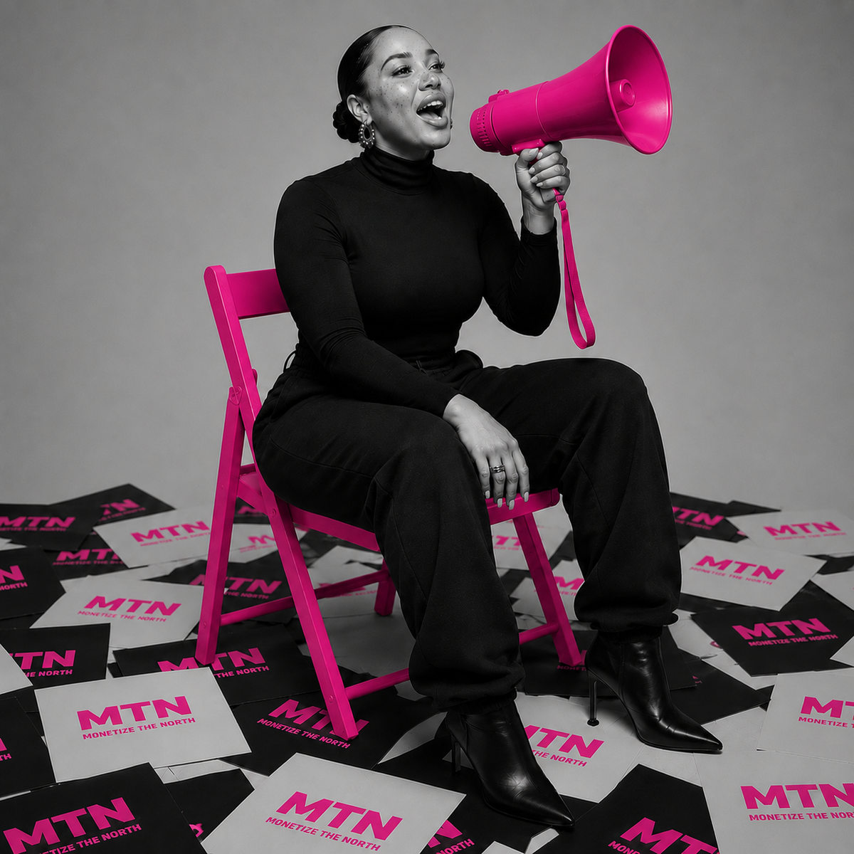 A woman sitting on a pink chair speaking into a matching pink megaphone, surrounded by scattered MTN campaign posters on the ground.